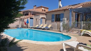 Uma piscina com espreguiçadeiras, uma área cercada e um edifício com telhado em azulejos.