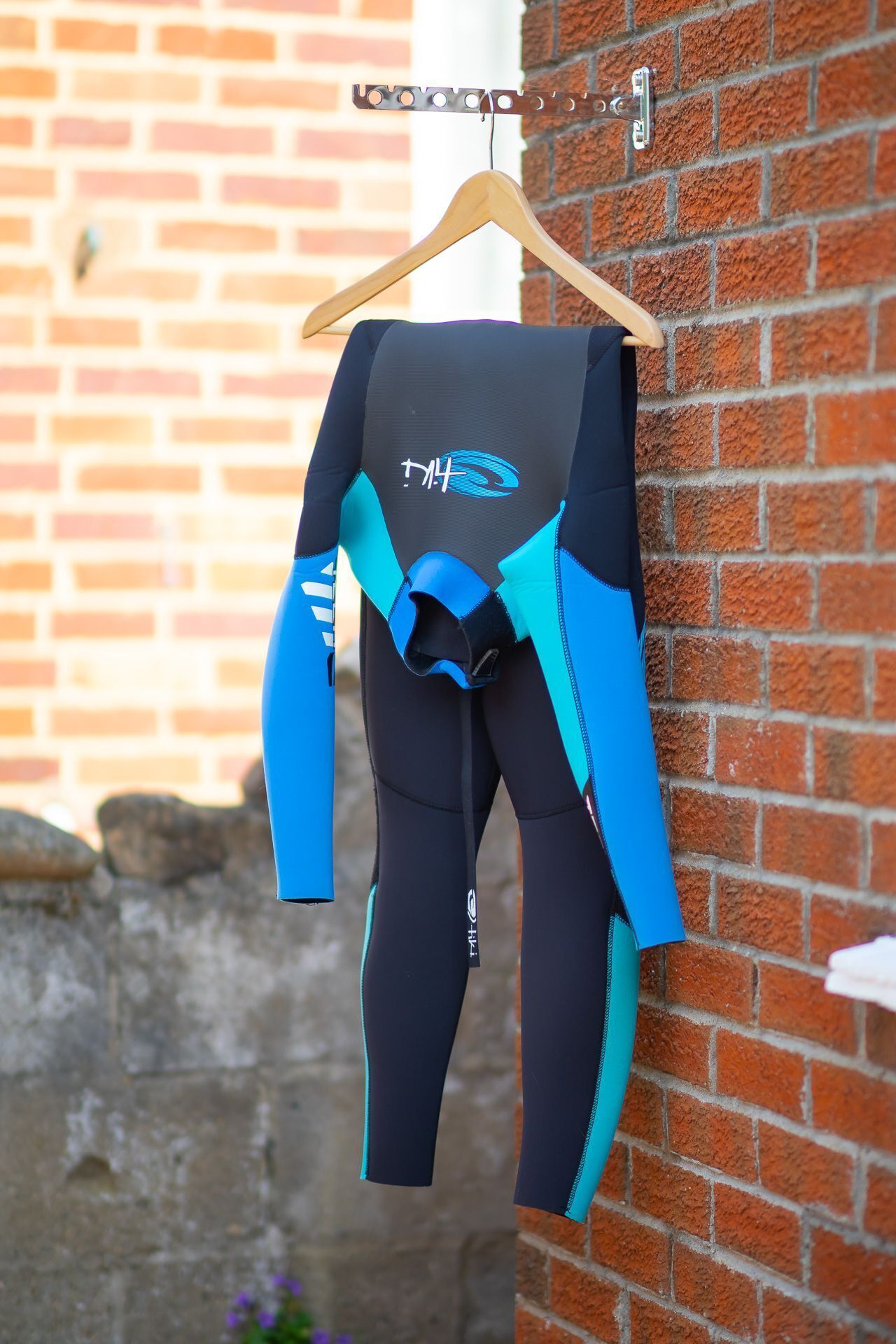 A wetsuit hanging on a wooden hanger against a brick wall.