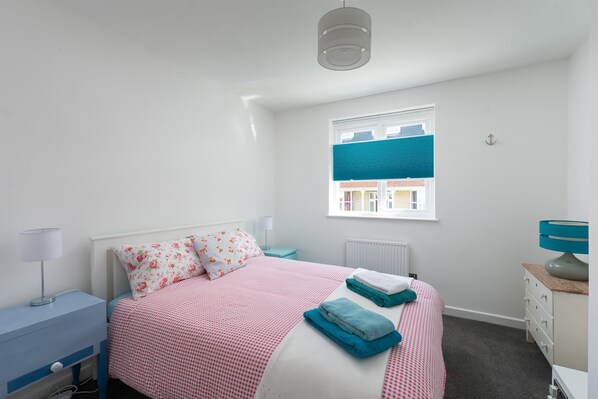 A bedroom with a bed, a nightstand, a lamp, a dresser, and a window with blinds. - Beach, dog and family friendly holiday home sleeping up to 6 in Combe Martin (Combe Martin, Ilfracombe)