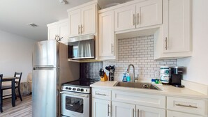 A modern kitchen with white cabinets, stainless steel appliances, a black countertop, and a tiled backsplash. - Walk to Sandfest , Shared Pool, Board Walk to Beach (Port Aransas)