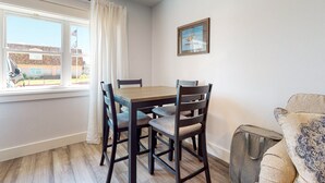 A dining area with a wooden table and chairs, a window with curtains, and a framed picture on the wall. - Walk to Sandfest , Shared Pool, Board Walk to Beach (Port Aransas)