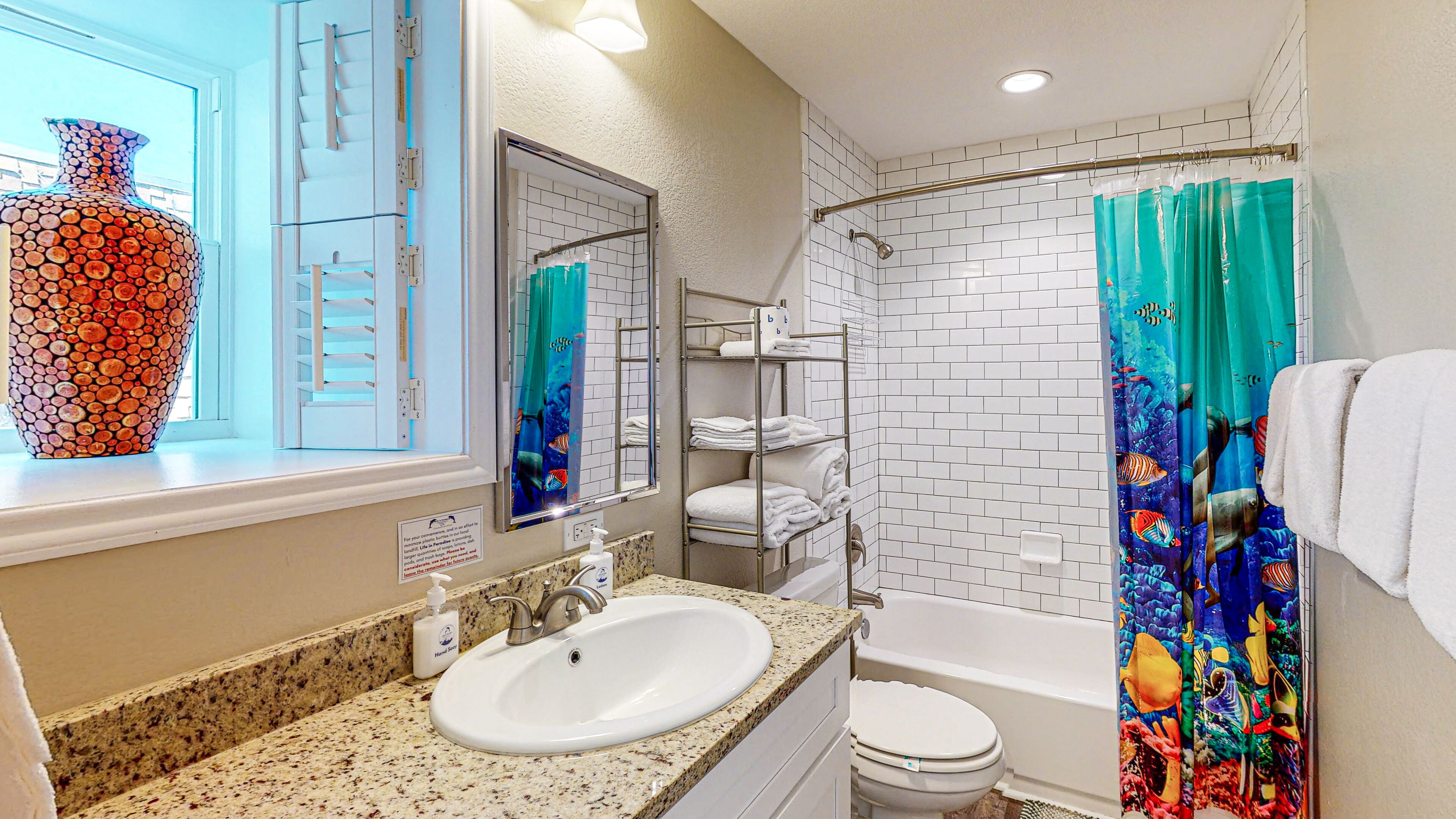 A bathroom with a white sink, a toilet, a bathtub, and a shower curtain with a fish pattern.