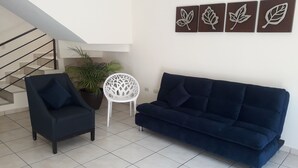A living room with a dark blue sofa, a white chair, and a potted plant. - Casa Vacacional en la Playa (Mazatlán)