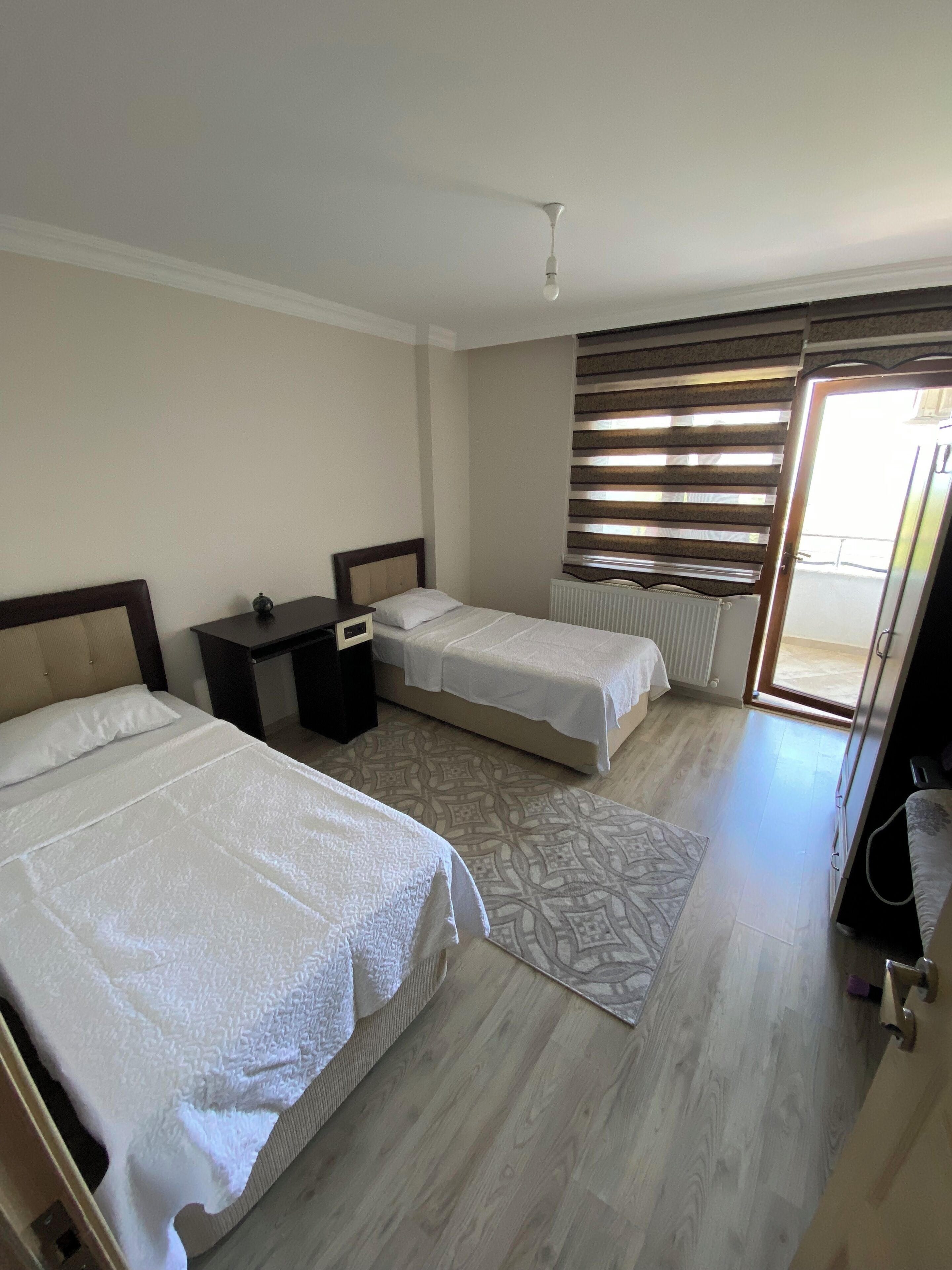 Quarto com duas camas, mesa de cabeceira, radiador e janela com persianas.
