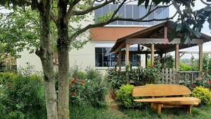 A wooden bench in a garden with a gazebo, surrounded by lush greenery and red flowers. - Menekse Apart 2 (Trabzon)