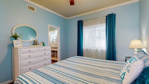 Quarto com cama, cômoda, espelho e janela com cortinas.