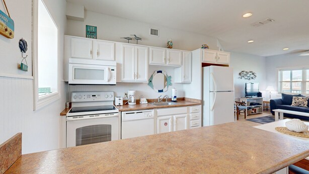 A kitchen with white cabinets, a granite countertop, and a dining area with a blue sofa. - Walk to Sandfest, Shared Pools, Boardwalk to Beach (Port Aransas)