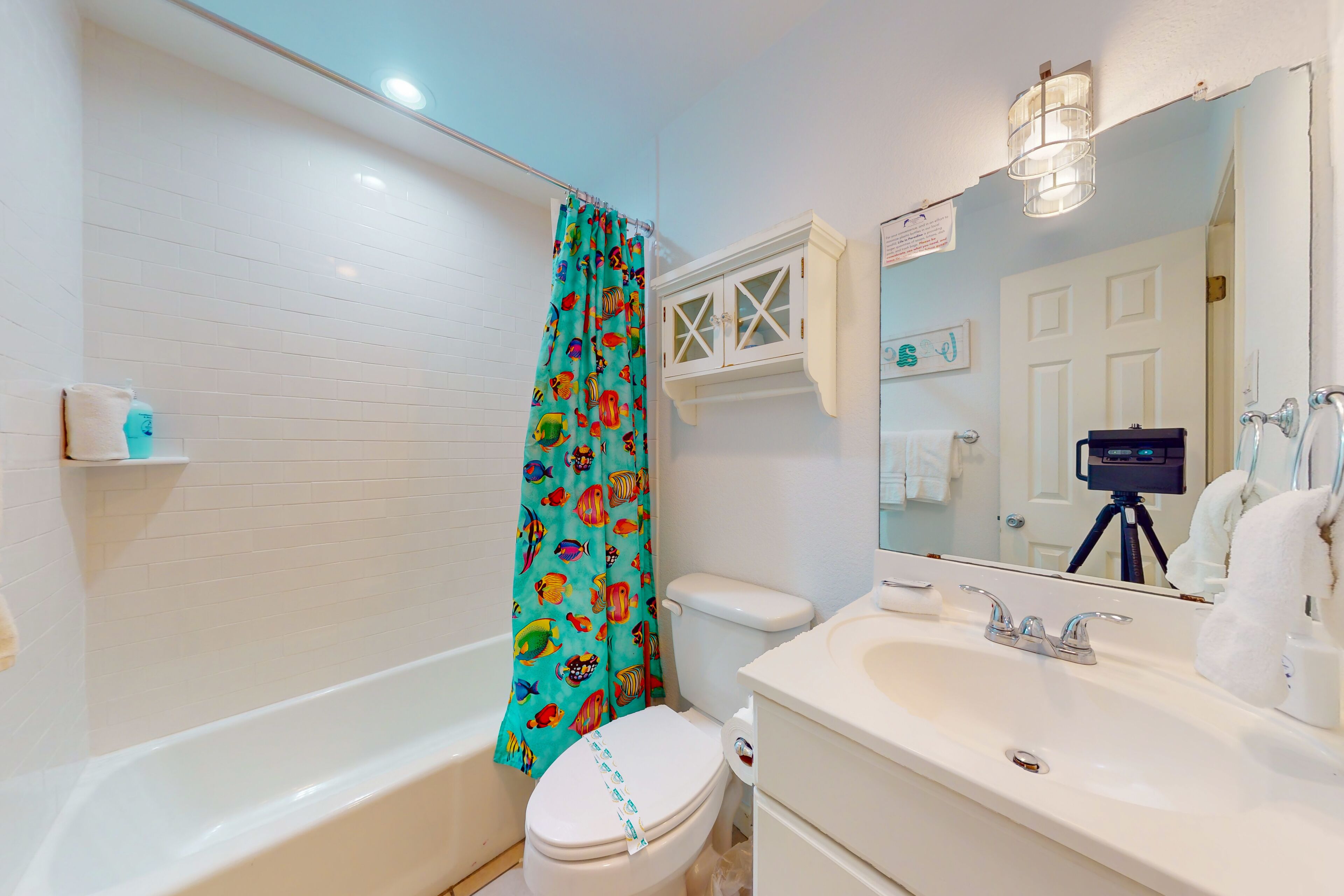 A bathroom with a white bathtub, a toilet, a sink with a mirror, and a shower curtain with a fish pattern.
