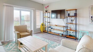 A living room with a ceiling fan, a TV mounted on the wall, and a wooden coffee table. - Walk to Sandfest, Shared Pools, Board Walk to Beach (Port Aransas)