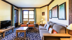Camera d'albergo con una grande televisione a schermo piatto, un divano, due poltrone, un tavolino da caffè e una tappezzeria decorata.