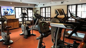 Una palestra con diverse tapis roulant, cyclette e un televisore che mostra un canale di notizie.