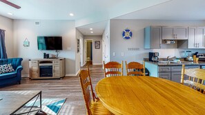 Uma sala de estar moderna com um sofá azul, uma mesa de jantar de madeira e uma cozinha com armários cinza e bancada azul.