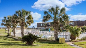 A residential area with palm trees, a white picket fence, and a house with a balcony. - Walk to Sandfest , Shared Pool, Board Walk to Beach (Port Aransas)