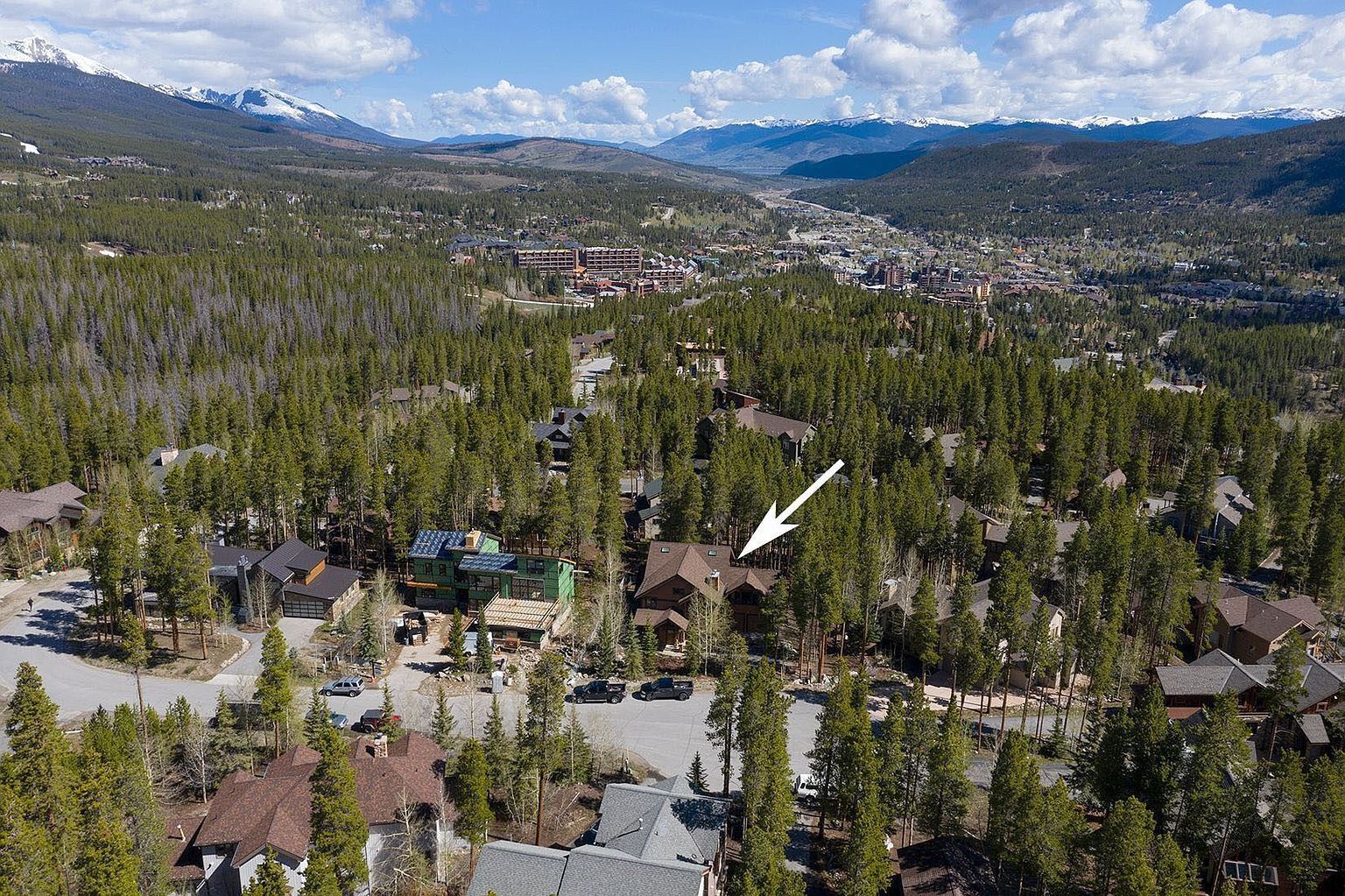 A residential area with houses surrounded by dense forests and mountains in the background.