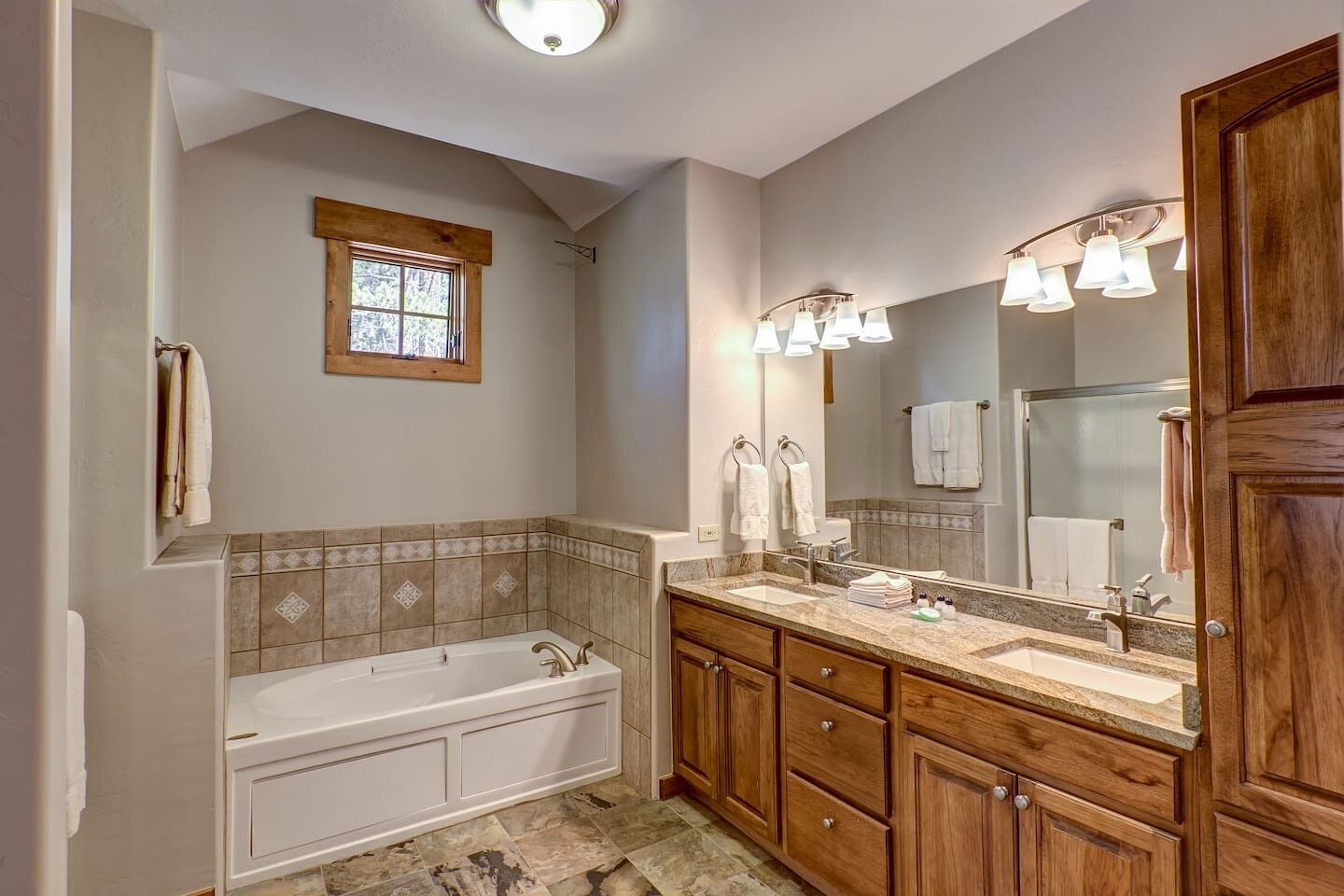 A bathroom with a bathtub, vanity with a mirror, and wooden cabinets.