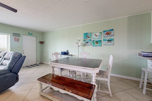 Uma área de refeições com mesa e cadeiras brancas, um banco e um ventilador de teto.
