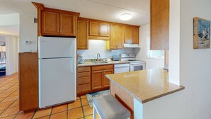 A kitchen with wooden cabinets, a refrigerator, a sink, and a countertop. - Walk to Sandfest,  Shared Pools, Boardwalk to the Beach (Port Aransas)