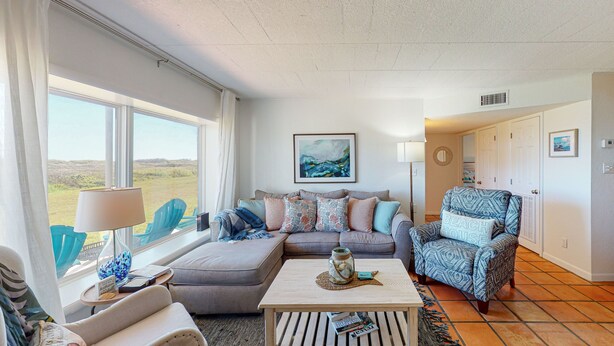 A living room with a sofa, armchair, and coffee table, a view of the outdoors, and a painting on the wall. - Walk to Sandfest,  Shared Pools, Boardwalk to the Beach (Port Aransas)