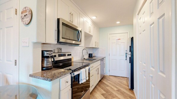 A kitchen with white cabinets, a microwave, a coffee maker, and a refrigerator.