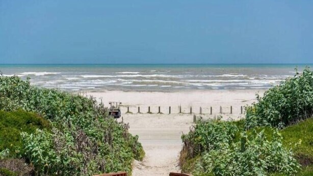 A beach with a pathway leading to the water, surrounded by greenery. - Walk to Sandfest, Shared Pool, Boardwalk to the Beach (Port Aransas)
