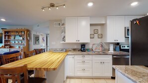 Une cuisine moderne avec des meubles blancs, une table à manger en bois et un réfrigérateur noir.