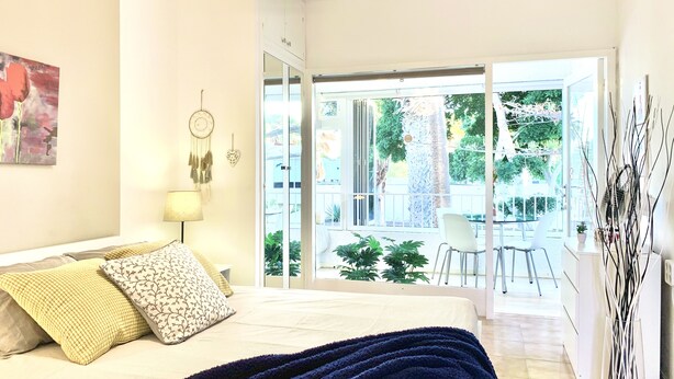 A bedroom with a bed, bedside table, lamp, and a view of the outdoors through a sliding glass door.