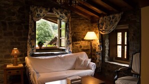 A cozy room with a stone wall, a white sofa, a wooden table, a lamp, and a chair. - Molino de Yera (Vega de Pas)