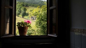 A window with a view of a rural landscape, including trees and a small house. - Molino de Yera (Vega de Pas)
