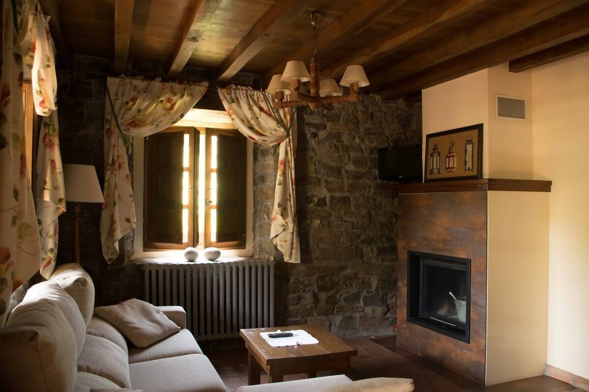Uma sala de estar aconchegante com parede de pedra, lareira, sofá e janela com cortinas.