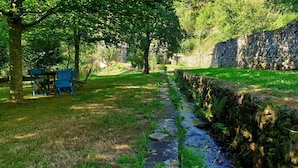 A stone wall, a narrow stream, and a grassy area with a bench and chairs. - Molino de Yera (Vega de Pas)
