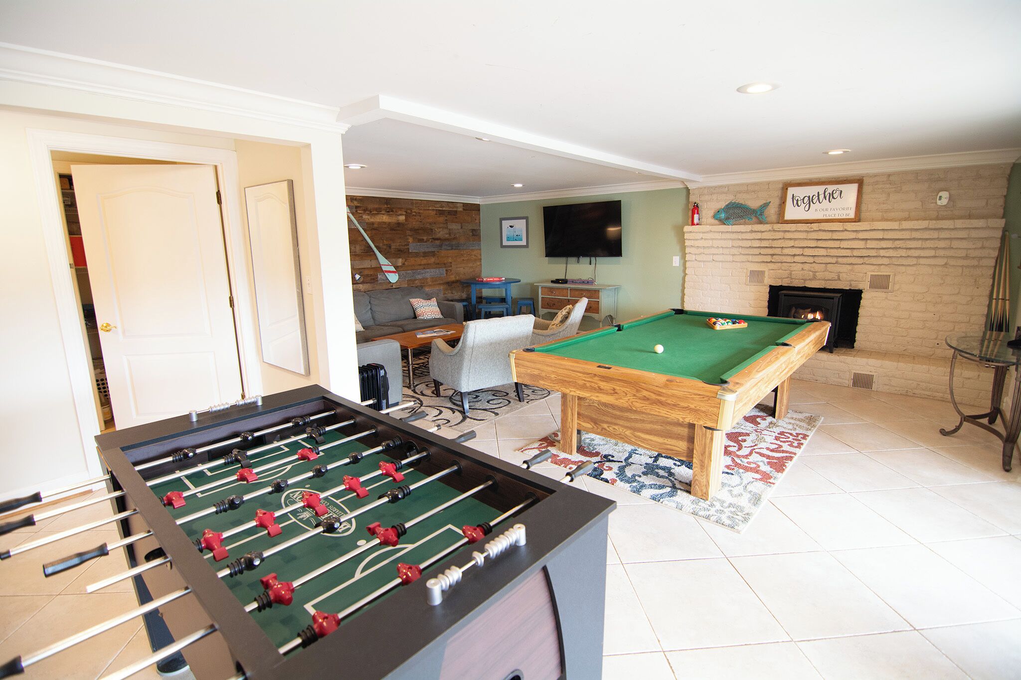 Een kamer met een tafelvoetbaltafel, een biljarttafel, een open haard en een televisie aan de muur.