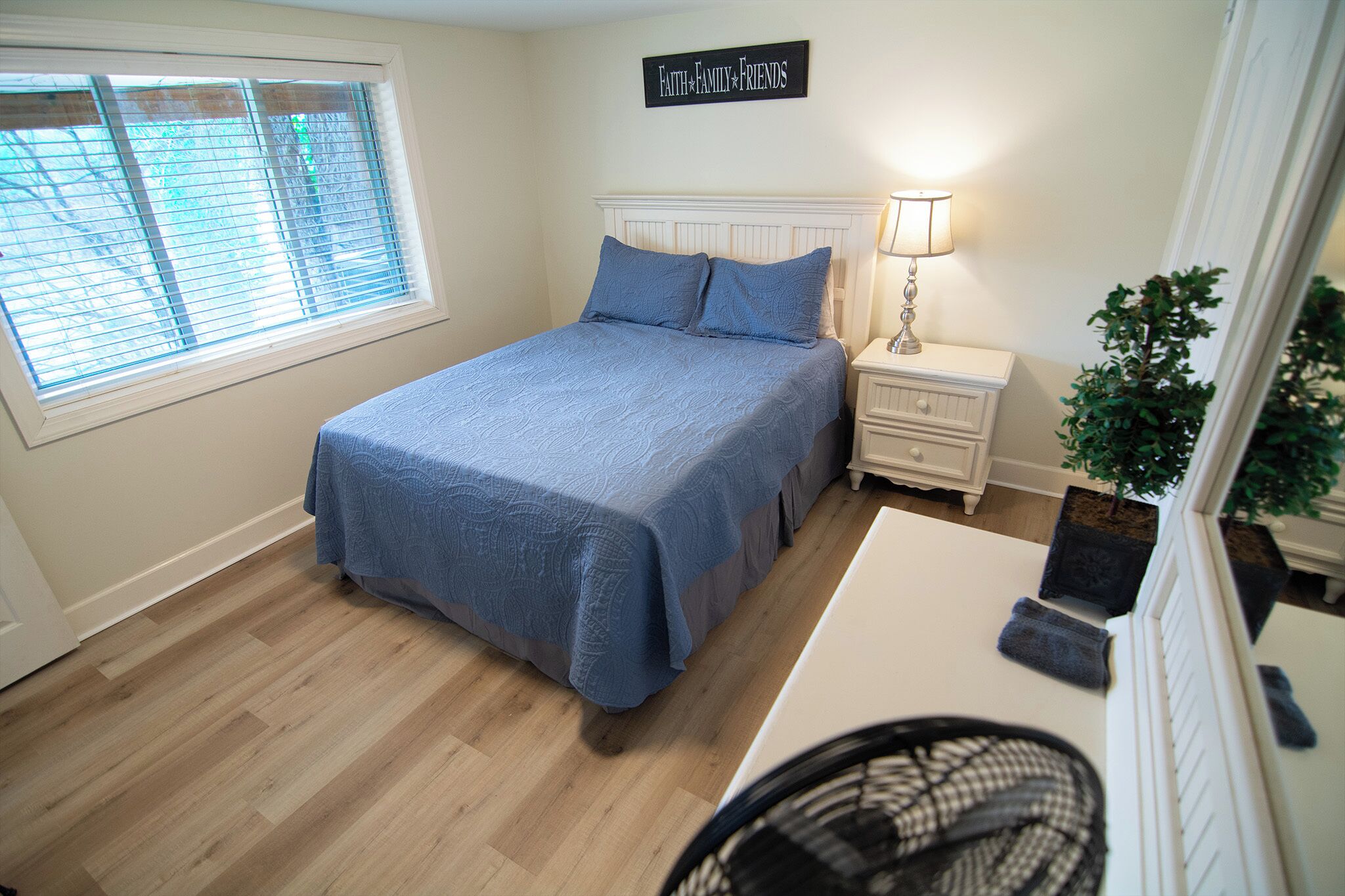 A bedroom with a bed, bedside table, lamp, and a sign on the wall.