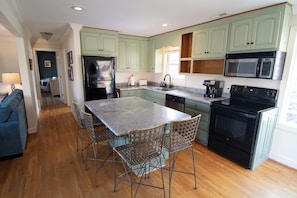 A kitchen with a central island, bar stools, a refrigerator, a microwave, and an oven.