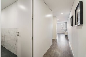 Un couloir aux murs blancs, avec un mur recouvert de carreaux de marbre et un plancher en bois.
