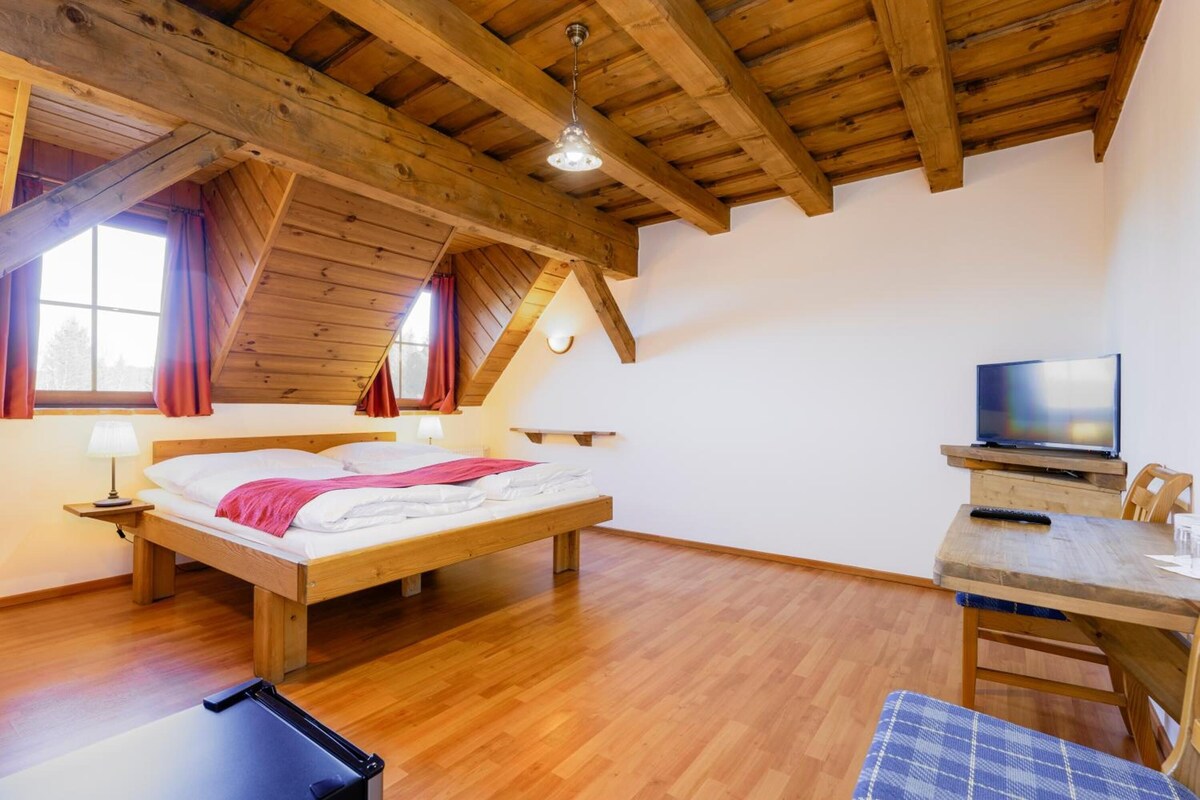 A room with a wooden ceiling, a bed, a TV, and a table with a chair.