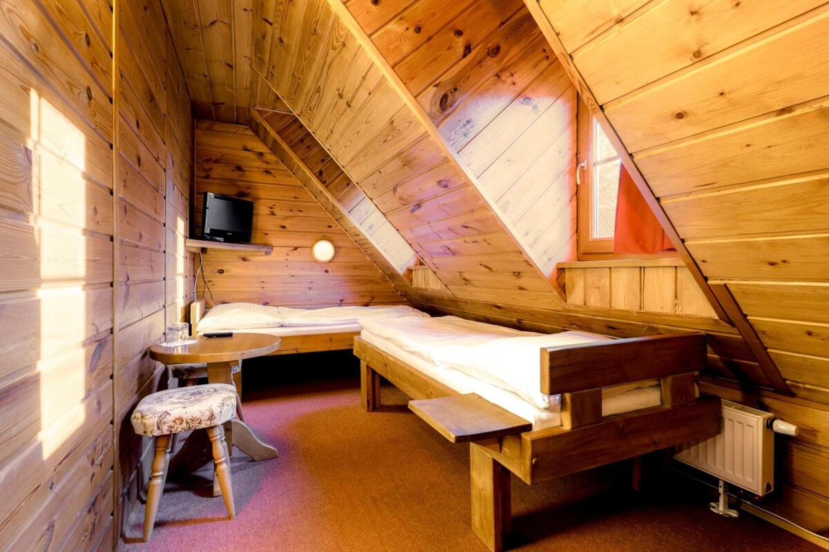 A small, cozy attic bedroom with a single bed, a small table, a chair, and a television.