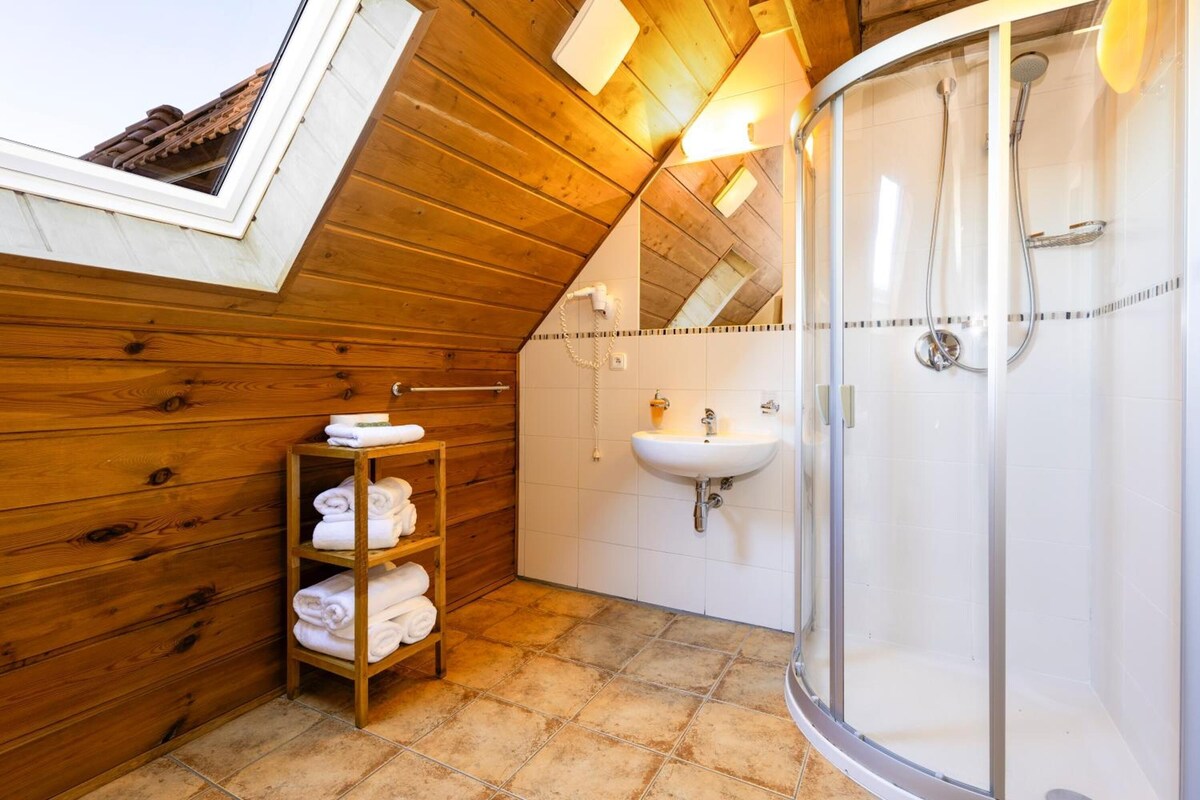 A wooden interior with a shower, a sink, and a shelf with towels.