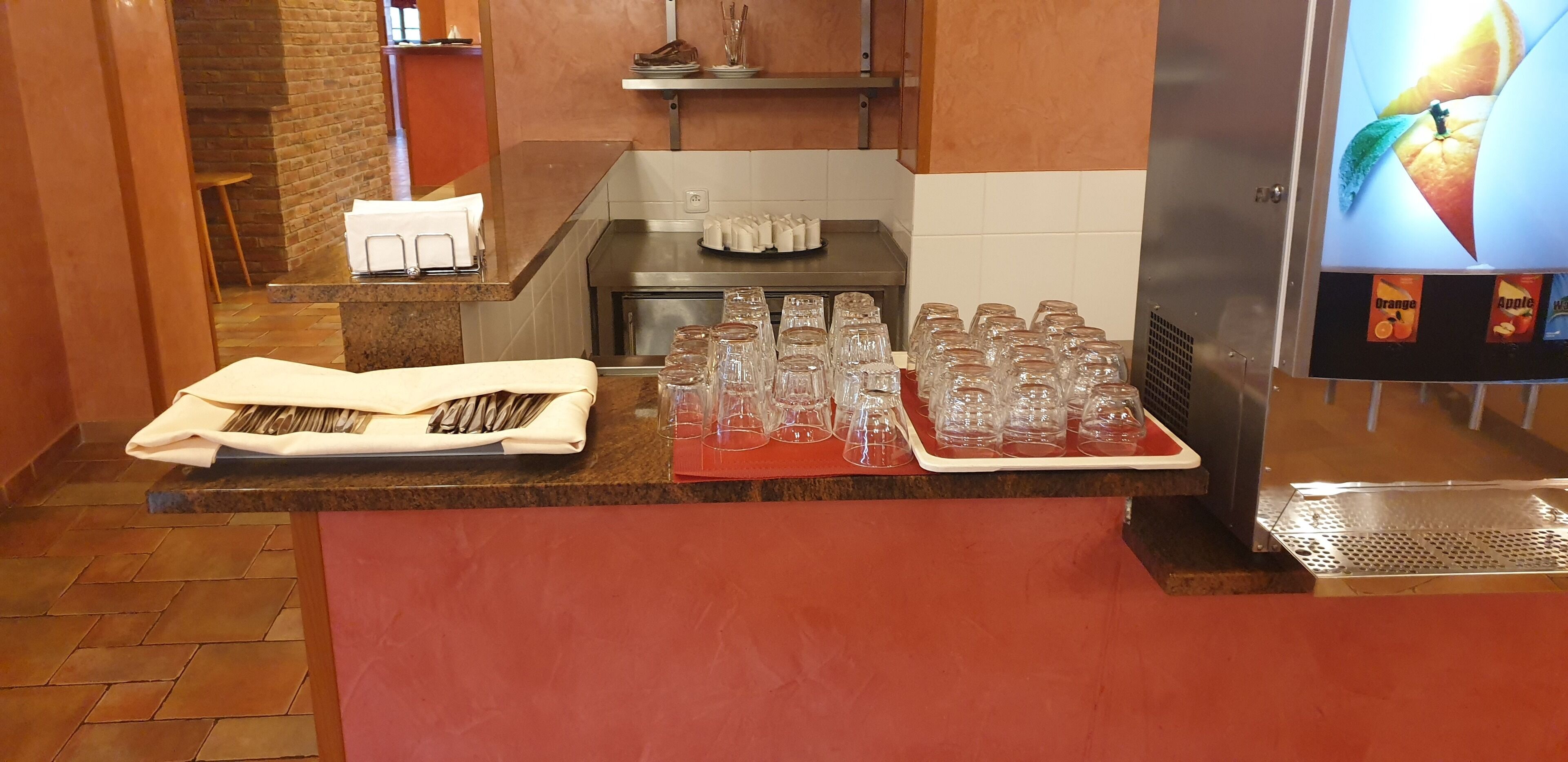 A hotel kitchen counter with glassware, a coffee machine, and a refrigerator.