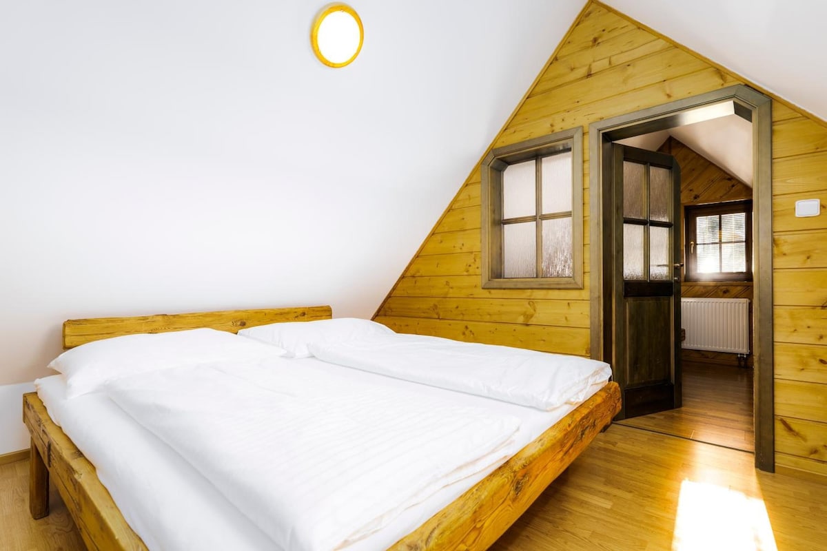 A bedroom with a wooden bed, a window, and a door leading to another room.