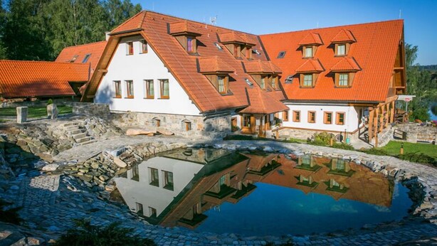 A traditional building with a sloped roof and multiple windows, reflecting in a pond.