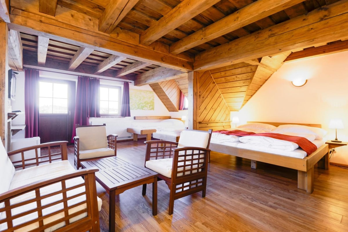 A cozy room with a wooden ceiling, a bed, a desk, and two chairs.