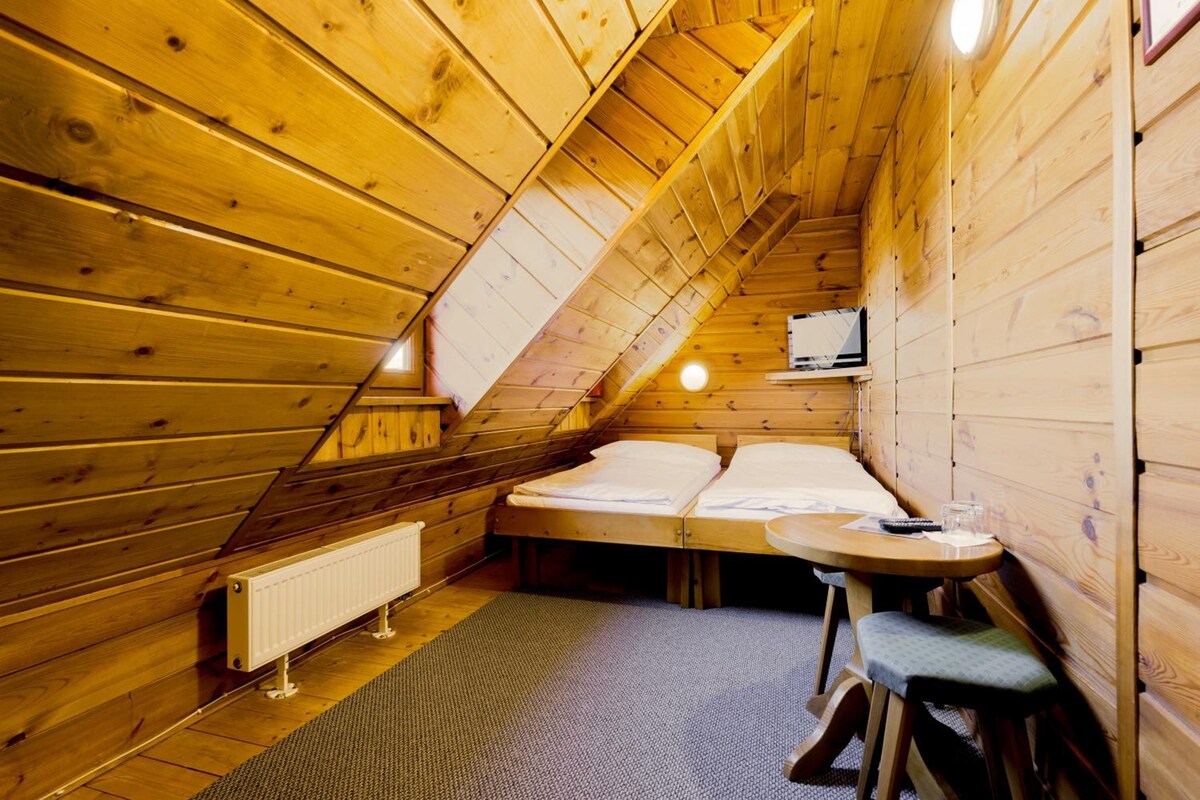 Ein kleines, gemütliches Schlafzimmer im Dachgeschoss mit schrägen Wänden, einem Einzelbett, einem kleinen Tisch und einer Heizung.