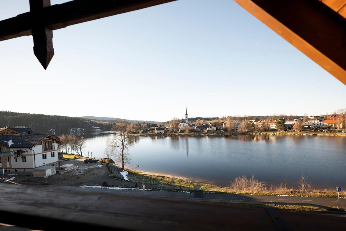 A view of a lake with a church and residential buildings in the background.