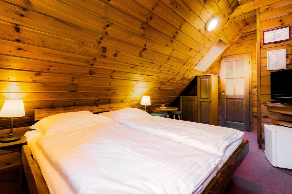 A wooden cabin bedroom with a bed, two bedside lamps, a television, and a small table.