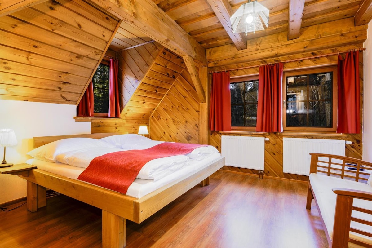 A wooden cabin with a bed, a table, and a window with curtains.