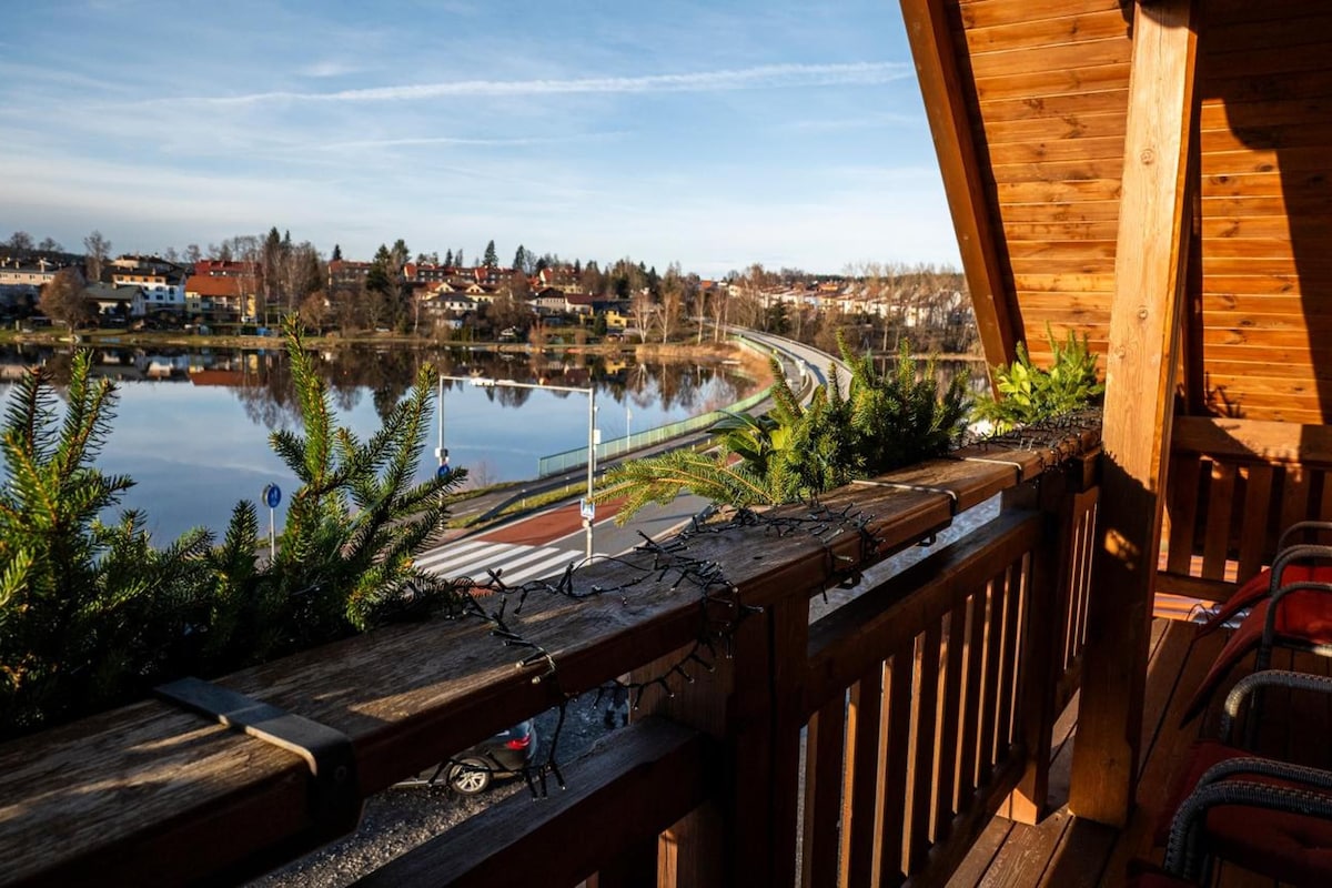 A wooden balcony with a view of a lake and a town in the background.