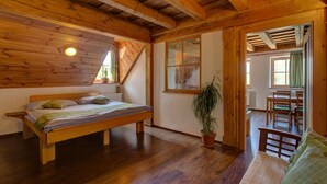 A wooden room with a bed, a potted plant, and a dining area with chairs and a table.
