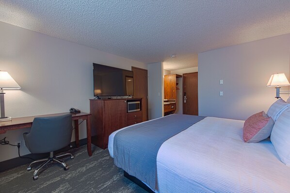 A hotel room with a bed, desk, chair, and a mirror.