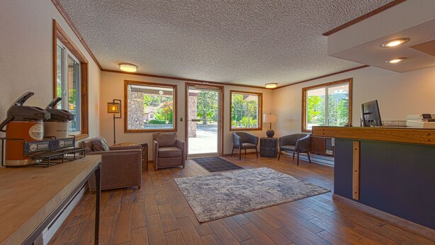 A spacious room with a wooden floor, a large rug, a seating area with chairs, a counter with a coffee machine, and large windows offering a view of the outdoors. - Silver Inn (Kellogg)