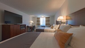 A hotel room with a large bed, a TV, a desk, and a window with curtains. - Silver Inn (Kellogg)